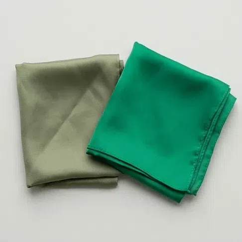 A muted moss green scarf folded beside a clean emerald one