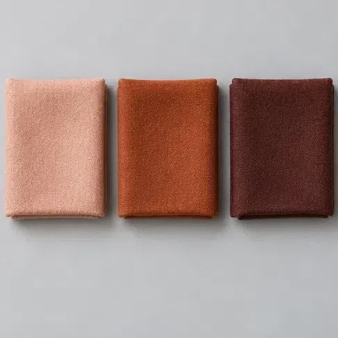 A light soft peach fabric square beside a rust and a deep mahogany one