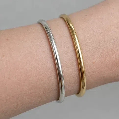 A polished silver bangle and a yellow gold one resting on a cool-toned forearm
