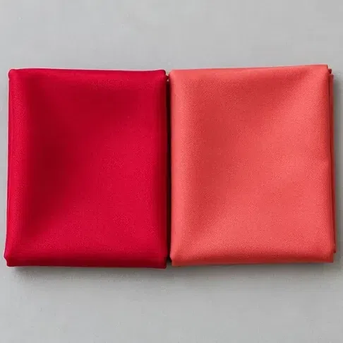 A clean blue-based red silk square beside a coral one of equal brightness
