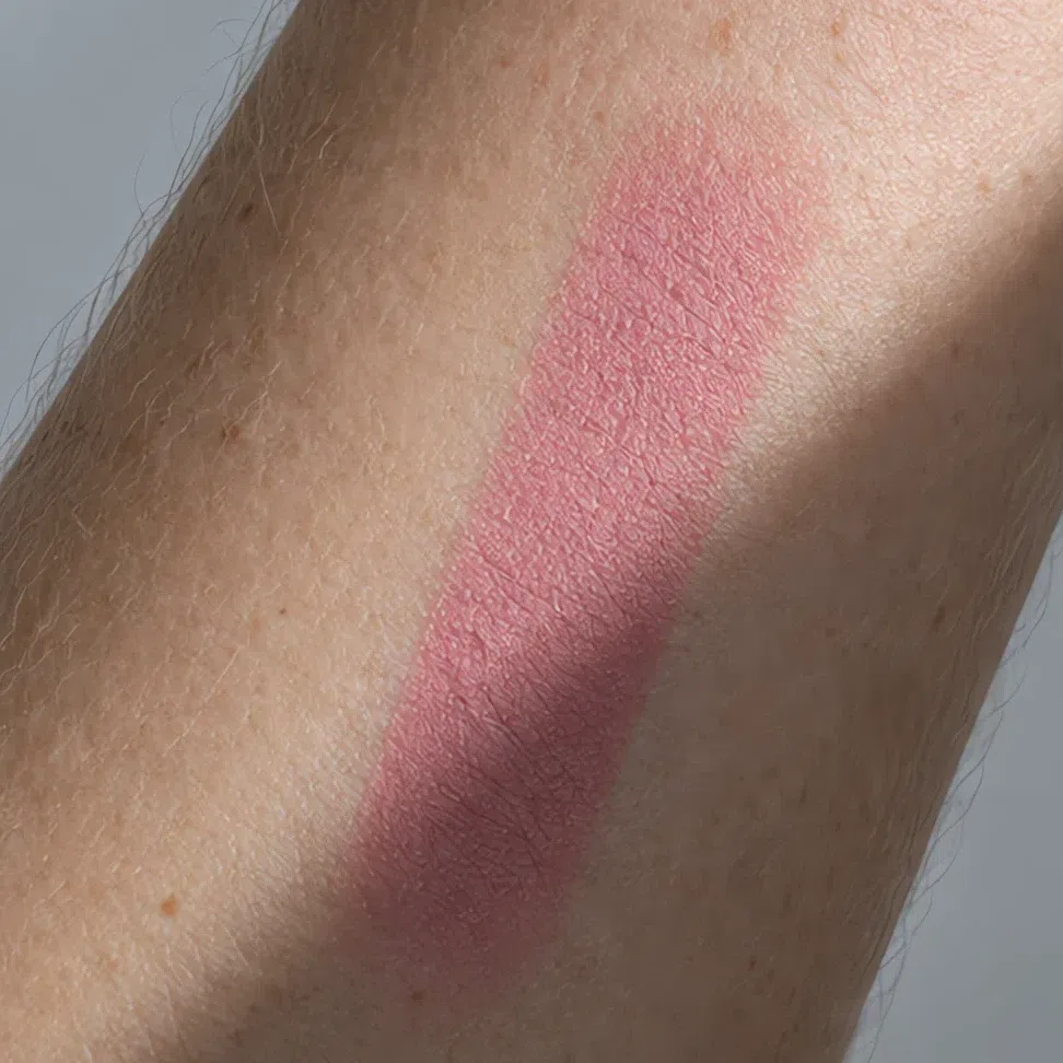 A cool rose blush stripe on a forearm in daylight, a shadow crossing part of the frame