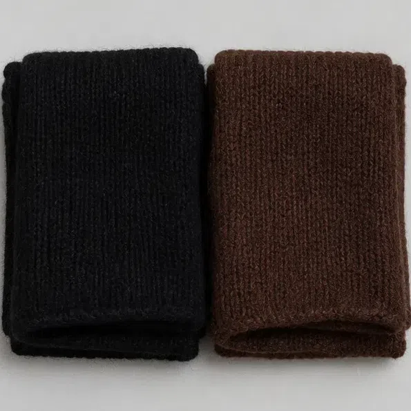 A jet black knit scarf folded next to a dark chocolate brown one of the same depth