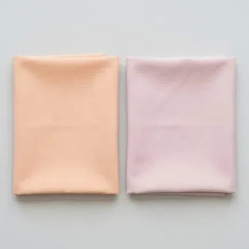 A light warm peach fabric square beside a light cool powder rose one