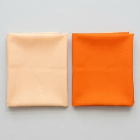 A soft apricot pastel fabric square beside a vivid saturated orange one