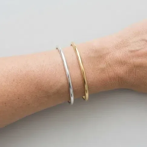 A silver bangle and a gold bangle resting on bare skin