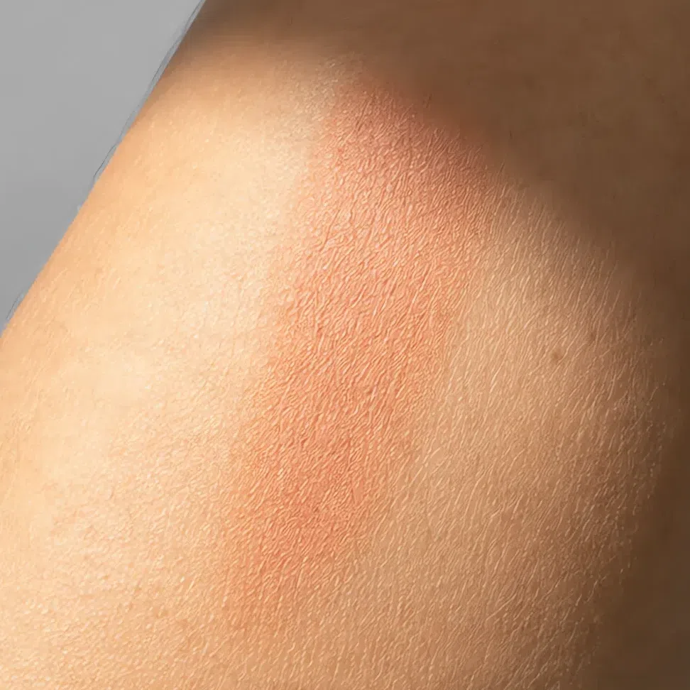A warm peach swatch in soft daylight with a shadow across it, reading true