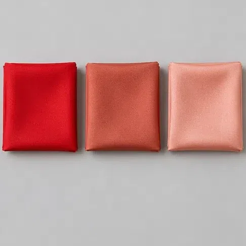A vivid tomato red fabric square beside a warm terracotta and a light peach-pink one