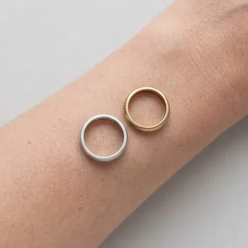 A matte silver band and an antiqued gold band on bare skin