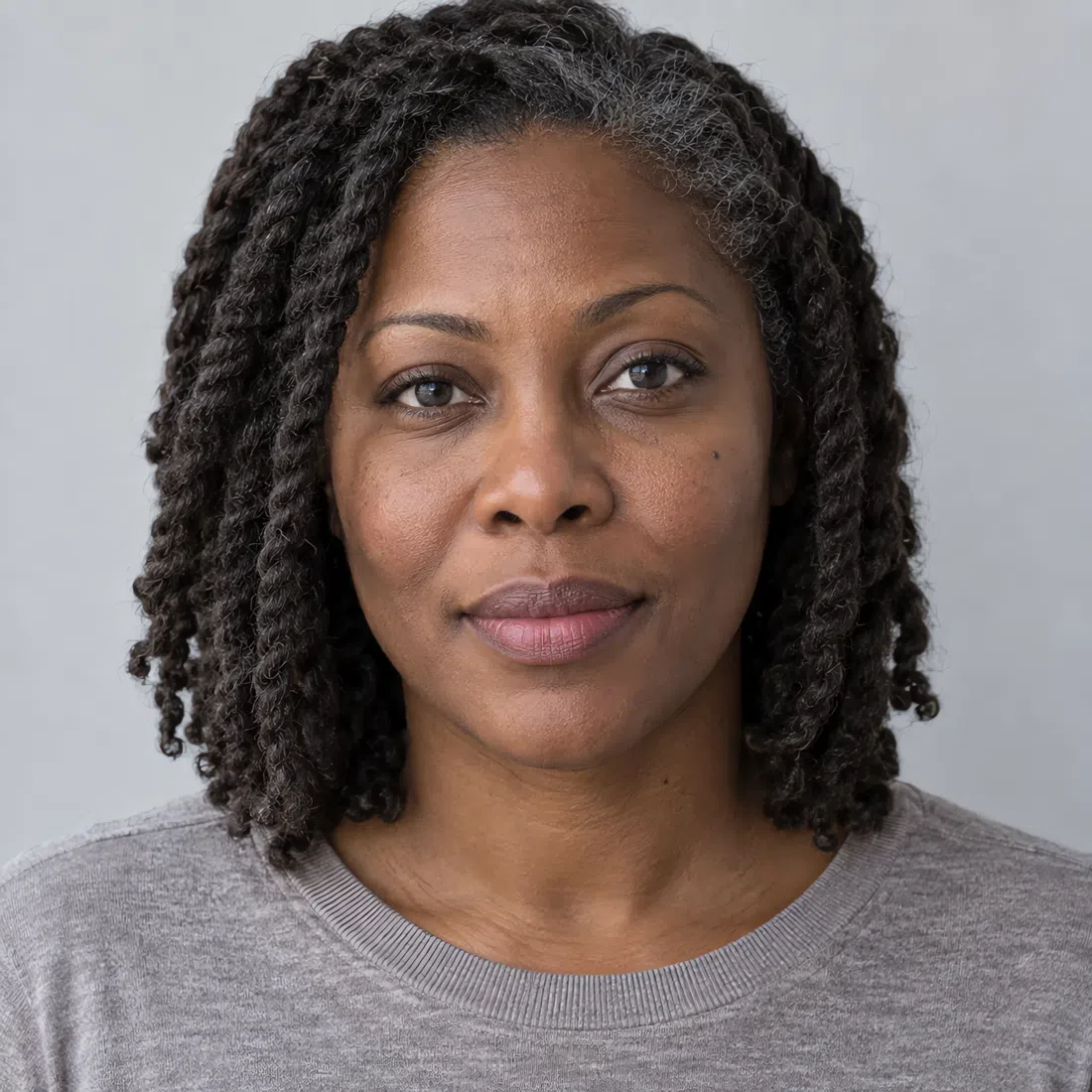 A Cool Summer woman with deep brown skin, dark eyes and graying twists, wearing a simple gray sweater
