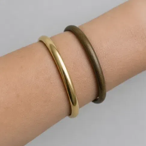 A polished yellow gold bangle and an antiqued bronze one lying on a bare forearm