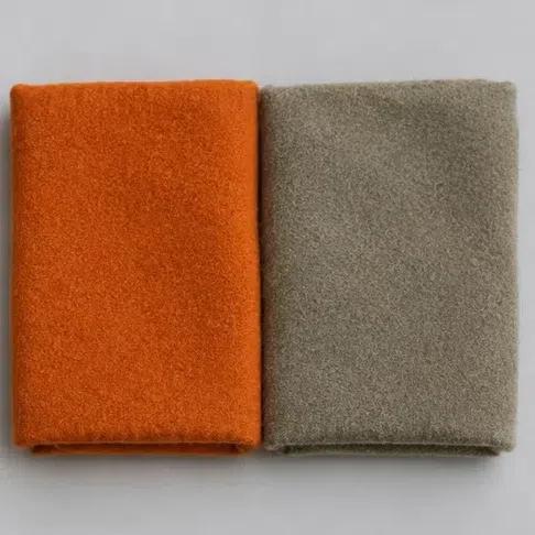 A saturated pumpkin-orange wool square next to a grayed khaki one