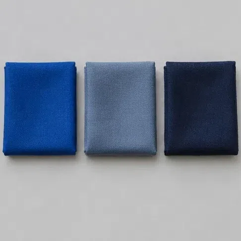 A pure royal blue fabric square beside a dusty blue-gray and a deep inky navy one