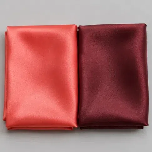 A clear coral silk square beside a deep burgundy one, for the drape comparison